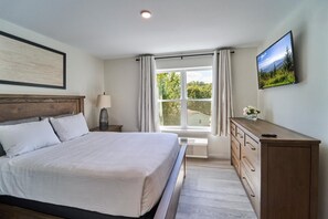 Quarto com cama, penteadeira, televisão e janela com cortinas.