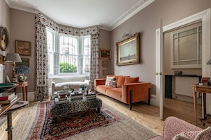 A living room with a sofa, a patterned rug, a window with curtains, and a painting on the wall. - Radipole Road IV - Three Bedroom House, Sleeps 6 (London)