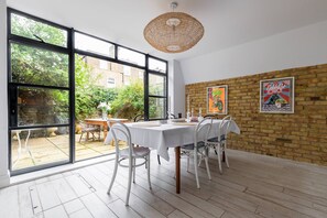 A dining area with a large window, a brick wall, and a hanging light fixture. - Radipole Road IV - Three Bedroom House, Sleeps 6 (London)