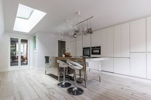 A modern kitchen with a skylight, stainless steel bar stools, and white cabinetry. - Radipole Road IV - Three Bedroom House, Sleeps 6 (London)