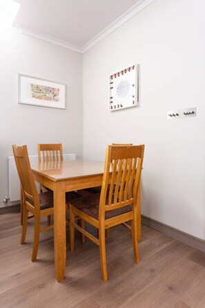 A dining table with four wooden chairs, white walls, a framed picture, and a whiteboard. - Red Lion Square - Two Bedroom Apartment, Sleeps 4 (London)