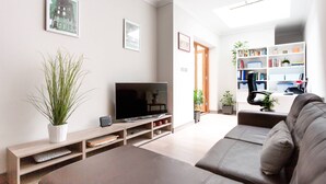 A modern living room with a flat-screen TV, a sofa, a bookshelf, and a potted plant. - Red Lion Square - Two Bedroom Apartment, Sleeps 4 (London)