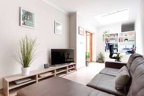 A modern living room with a flat-screen TV, a sofa, a bookshelf, and a potted plant. - Red Lion Square - Two Bedroom Apartment, Sleeps 4 (London)