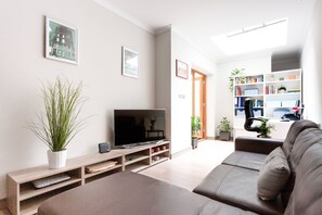 A modern living room with a flat-screen TV, a sofa, a bookshelf, and a potted plant. - Red Lion Square - Two Bedroom Apartment, Sleeps 4 (London)
