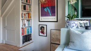 A room with a bookshelf, a framed artwork, a sofa with decorative pillows, and a television. - Royal Crescent Mews - One Bedroom House, Sleeps 2 (London)