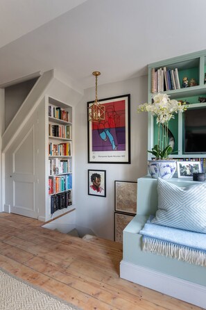 A room with a bookshelf, a framed artwork, a sofa with decorative pillows, and a television. - Royal Crescent Mews - One Bedroom House, Sleeps 2 (London)