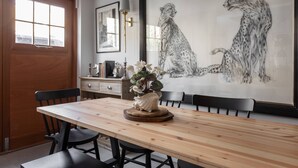 A dining area with a wooden table, chairs, a vase with flowers, a framed cheetah painting, and a window with a view. - Royal Crescent Mews - One Bedroom House, Sleeps 2 (London)