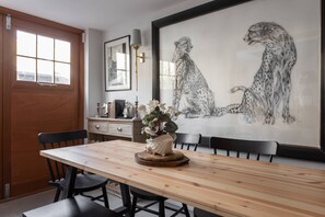 A dining area with a wooden table, chairs, a vase with flowers, a framed cheetah painting, and a window with a view. - Royal Crescent Mews - One Bedroom House, Sleeps 2 (London)