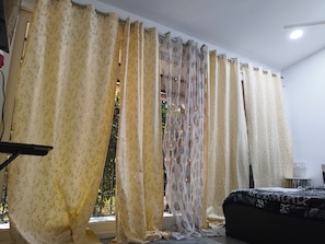 A room with a bed, a window with curtains, and a small table.