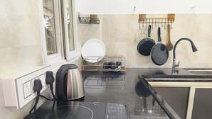 Eine Küche mit Einbau-Induktionskochfeld, einem Wasserkocher, einem Geschirrgestell und einer hängenden Kochutensilienstange.