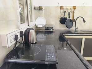 Uma cozinha com fogão por indução embutido, chaleira, escorredor de louça e suporte para pendurar panelas.