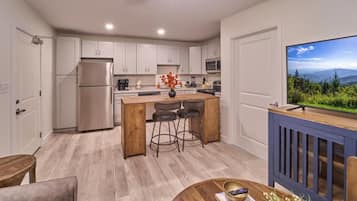 A modern kitchen with a large island, stainless steel appliances, and a view of a forest.
