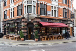 A corner building with 'The Larrik' signage, outdoor seating, and a large planter. - Wyndham Mews - Three Bedroom Apartment, Sleeps 6 (London)