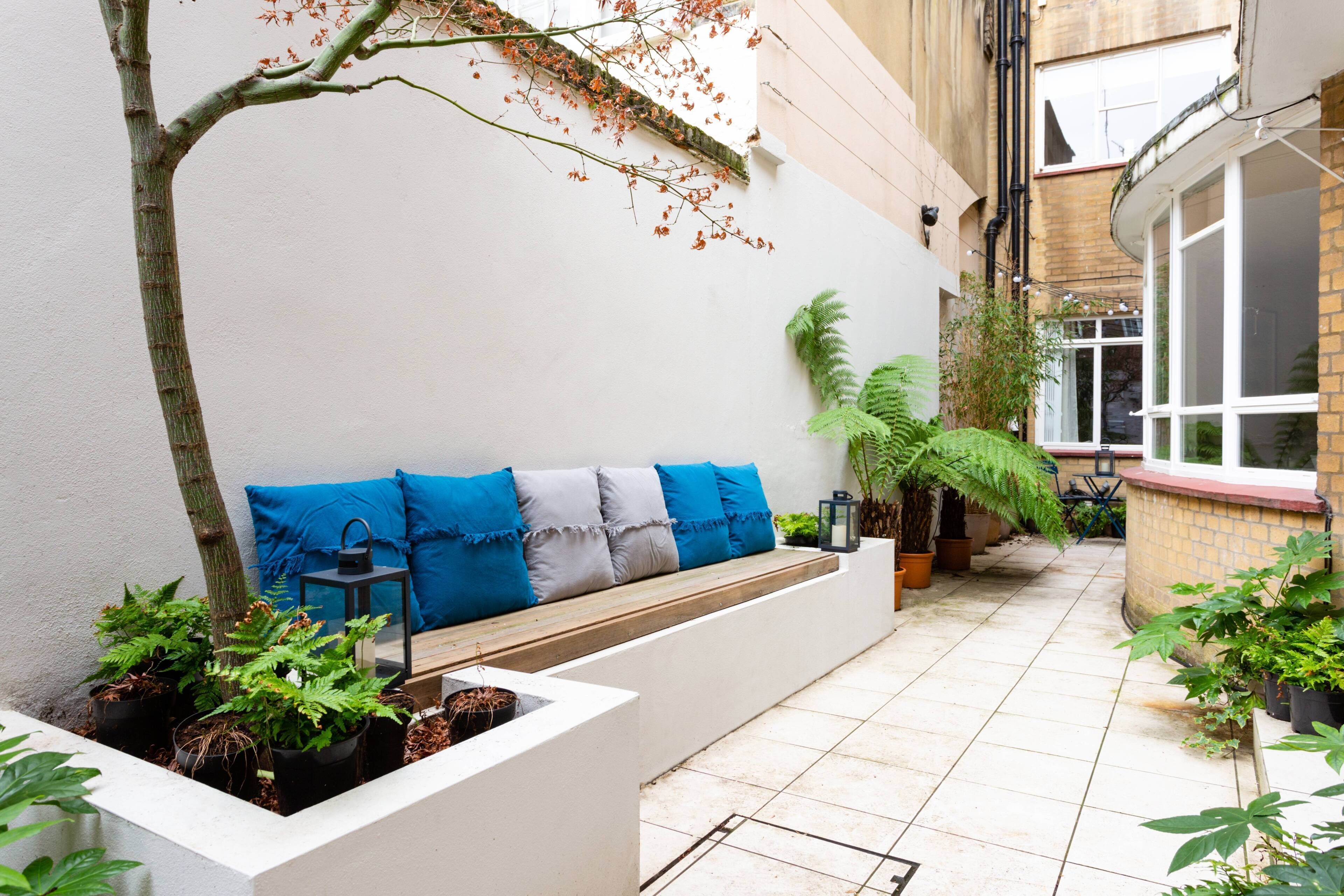 A courtyard with a bench, potted plants, and a tree.
