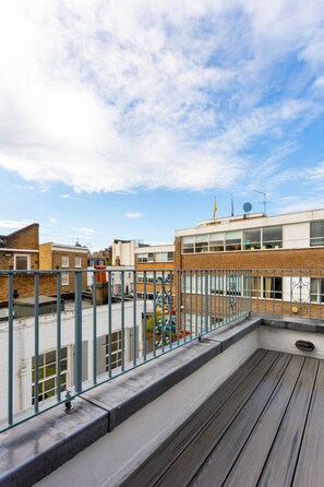 Eine Dachterrasse mit Holzboden, Metallgeländer und Blick auf umliegende Gebäude.