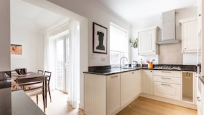 A modern kitchen with white cabinetry, a black countertop, and a dining area with a table and chairs. - Edge Street IV - Two Bedroom Apartment, Sleeps 3 (London)