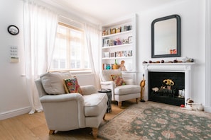 Ein Wohnzimmer mit zwei Sesseln, einem Bücherregal, einem Kamin und einem Spiegel.