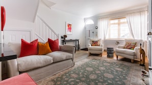 A living room with a sofa, two armchairs, a coffee table, a rug, a staircase, a door, and a window with curtains. - Edge Street IV - Two Bedroom Apartment, Sleeps 3 (London)