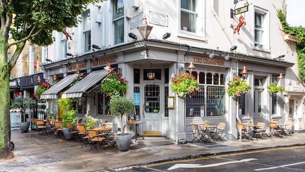 A building with 'The Champion' signage, outdoor seating with tables and chairs, and hanging flower baskets. - Edge Street IV - Two Bedroom Apartment, Sleeps 3 (London)