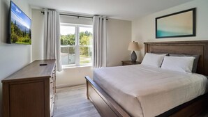 Ein Schlafzimmer mit Bett, Schreibtisch, Fernseher, einem Fenster mit Vorhängen und einem Bild an der Wand.