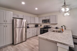 A modern kitchen with stainless steel appliances, white cabinetry, granite countertops, and a hanging light fixture. - The Ruby 314 (Pigeon Forge)