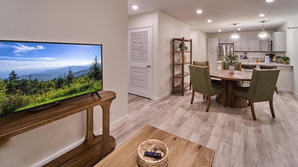 Eine moderne Küche mit Essbereich, einem an einer Holzkonsole montierten Fernseher und Blick auf eine Berglandschaft.