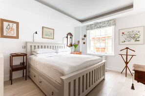 A bedroom with a bed, a nightstand, a dresser, a mirror, a window with a view, and wall art. - Tite Street VIII - One Bedroom Apartment, Sleeps 2 (London)