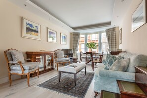 A living room with a sofa, armchairs, a coffee table, a rug, and a dining area with a table and chairs. - Tite Street VIII - One Bedroom Apartment, Sleeps 2 (London)