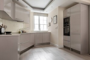 A modern kitchen with built-in appliances, a window with curtains, and a light-colored floor. - Tite Street VIII - One Bedroom Apartment, Sleeps 2 (London)