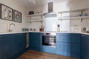 Eine moderne Küche mit blauen Schränken, weißen Arbeitsplatten, einem eingebauten Backofen und dekorativen Gegenständen auf Regalen.