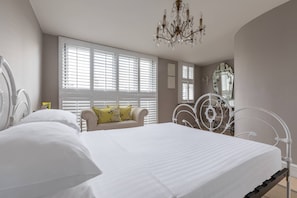 Ein Schlafzimmer mit einem großen Bett, einer Chandelier, einem Sessel mit Kissen und einem Spiegel.