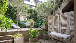 Un patio con plantas en macetas, un banco y una mesa con sillas.
