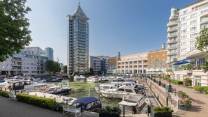 Un puerto deportivo con barcos amarrados, un edificio alto y un paseo marítimo.