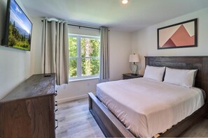 Une chambre à coucher avec un lit, une table de chevet, une lampe, un téléviseur et une fenêtre avec des rideaux.