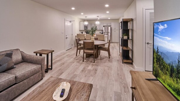 A modern living room with a sofa, coffee table, and TV. A dining area with a table and chairs is visible in the background. - The Ruby 315 (Pigeon Forge)