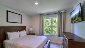 A bedroom with a bed, a nightstand, a dresser, a window with curtains, and a wall-mounted TV. - The Ruby 315 (Pigeon Forge)