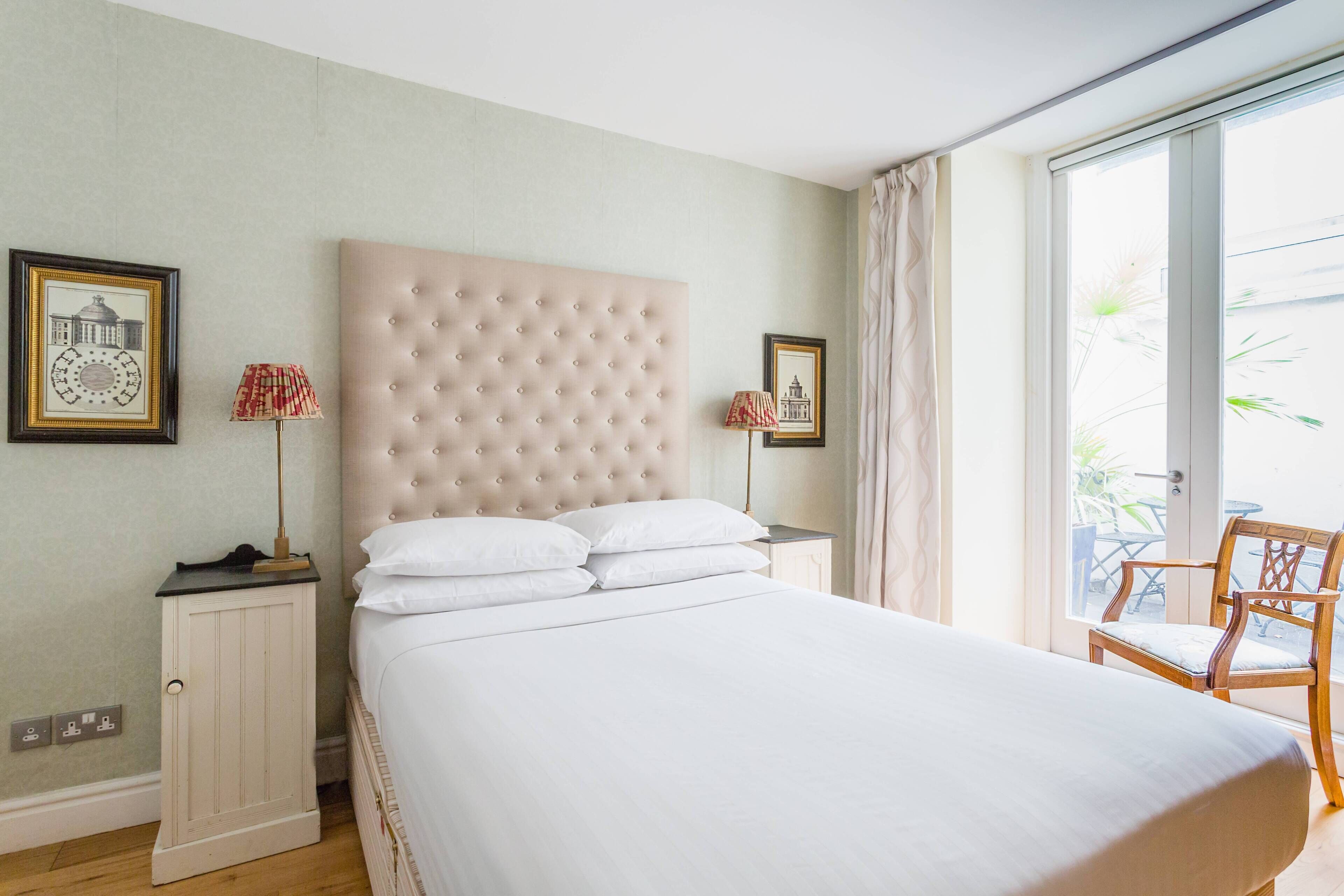 A bedroom with a large bed, a nightstand, a chair, and a view of the outside.