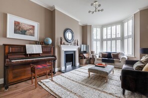 Ein Wohnzimmer mit einem Flügel, einem Kamin, einer Couch und einem großen Fenster.