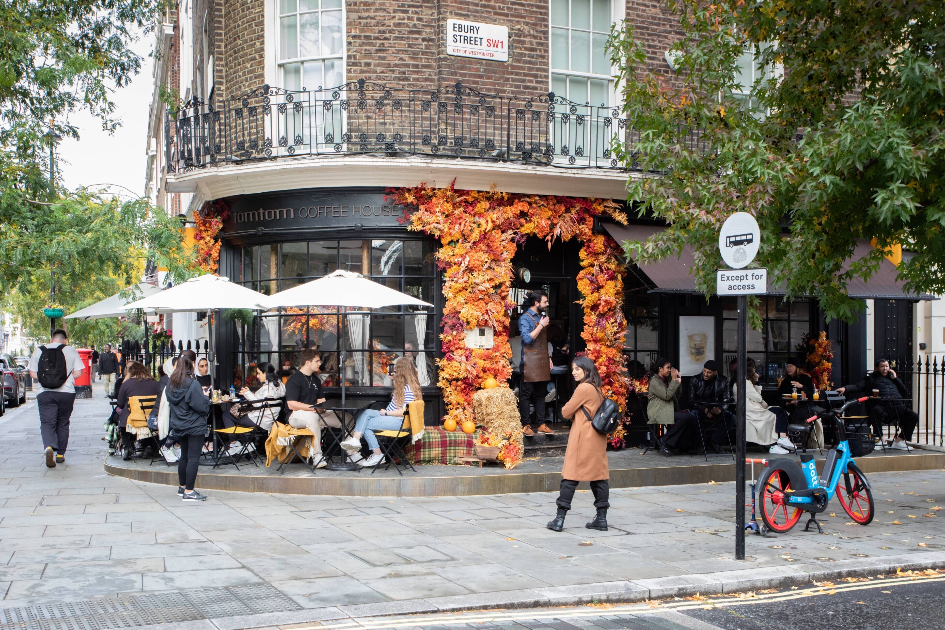 Un edificio con un cartel que dice 'EBURY STREET SW1' y una cafetería con mesas al aire libre.