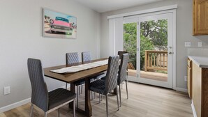 A dining area with a table and chairs, a painting on the wall, and a sliding glass door leading to an outdoor deck. - Rad Pad - Arcades, Seasonal Pool (Boise)