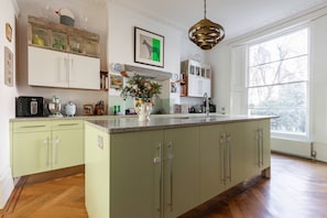 A kitchen with a central island, wooden flooring, and a large window. - Milborne Grove - Four Bedroom House, Sleeps 8 (London)