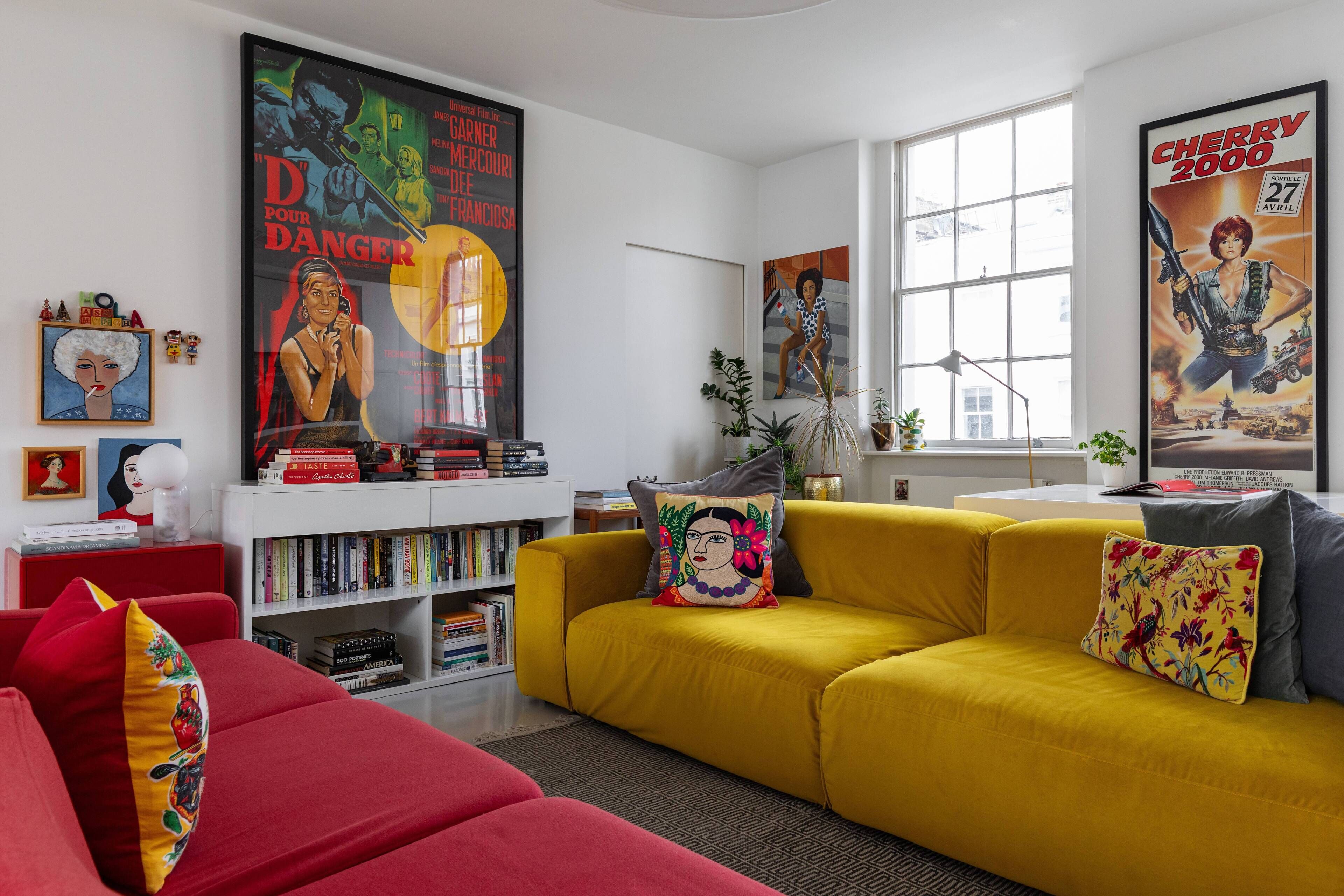 A modern living room with a yellow sofa, red couch, and a bookshelf filled with books.