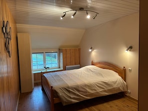 A bedroom with a wooden bed, a window with a view, and a ceiling fan. - House near the landing beaches Sainte Mere Eglise/Carentan (Boutteville)