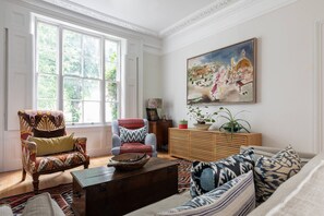 Ein Wohnzimmer mit großem Fenster, einer Couch, einem Sessel, einer Holzkabine und einem Gemälde an der Wand.