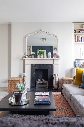 Ein Wohnzimmer mit Kamin, einem Couchtisch mit Büchern, einer Couch und einem Bücherregal.