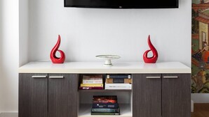 Ein modernes Wohnzimmer mit einem an der Wand befestigten Flachbildfernseher, einem weißen Konsolentisch mit zwei roten Vasen und einem Bücherregal mit Büchern.