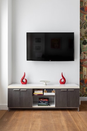 Ein modernes Wohnzimmer mit einem an der Wand befestigten Flachbildfernseher, einem weißen Konsolentisch mit zwei roten Vasen und einem Bücherregal mit Büchern.