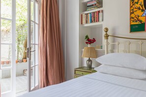 Ein Schlafzimmer mit Bett, Nachttisch mit Lampe, Bücherregal und Fenster mit Vorhängen.