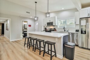 Una cocina moderna con una isla central, taburetes de bar, electrodomésticos de acero inoxidable y un cubo de basura.