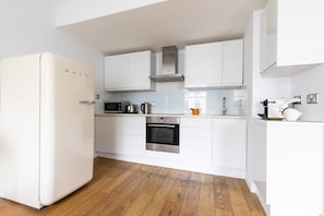 A kitchen with white cabinets, a stainless steel oven, a microwave, and a refrigerator. - St Stephen's Gardens VIII (London)